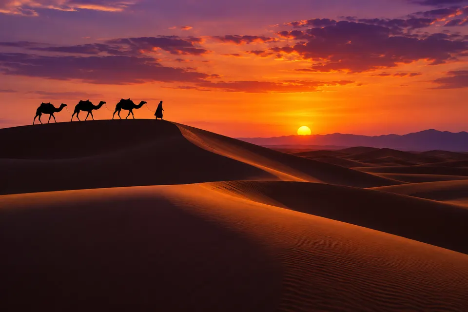 Desert sand dunes at dusk with long shadows and a lone camel caravan silhouette on the ridge, warm orange and violet sky