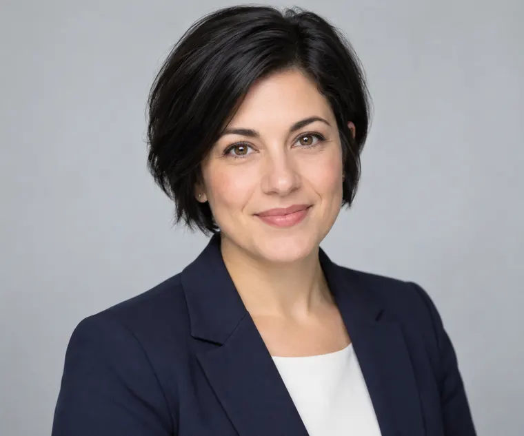 Professional headshot of an adult woman with short black hair in a navy blazer, light grey seamless background, soft even lighting, LinkedIn-style business portrait, original person