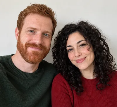 Input photo: a man with a red beard in a green sweater and a woman with curly black hair in a red sweater