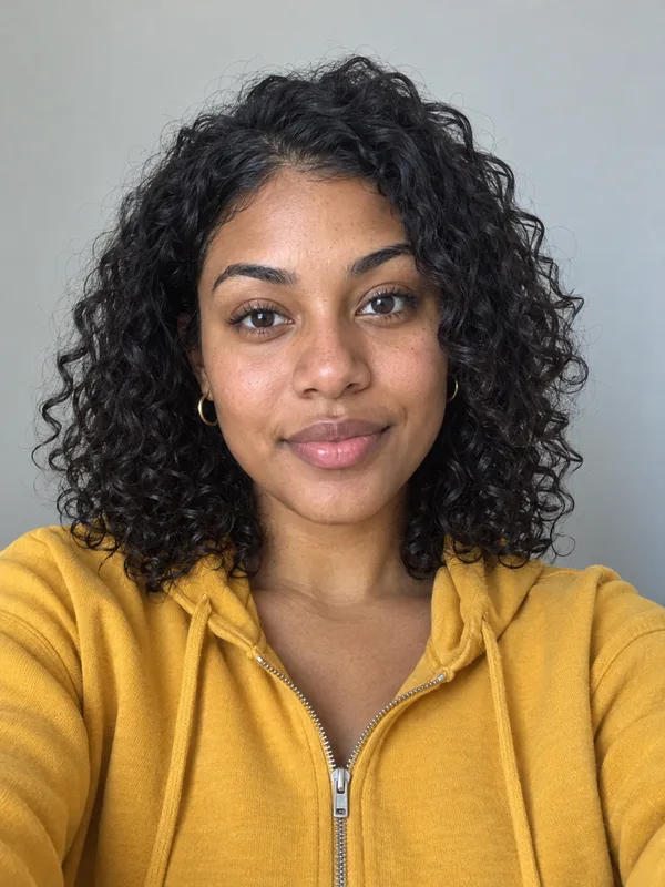 Input selfie: a woman with curly hair in a mustard-yellow hoodie