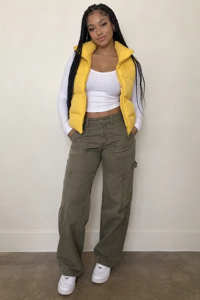 Foto de entrada: una mujer con trenzas largas, chaleco acolchado amarillo y pantalón cargo verde oliva, y una mujer de pelo rizado con sudadera negra con cremallera y leggings