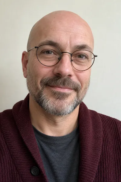 Eingabefoto: ein Mann in seinen 40ern mit Glatze, runder Brille und burgunderroter Strickjacke